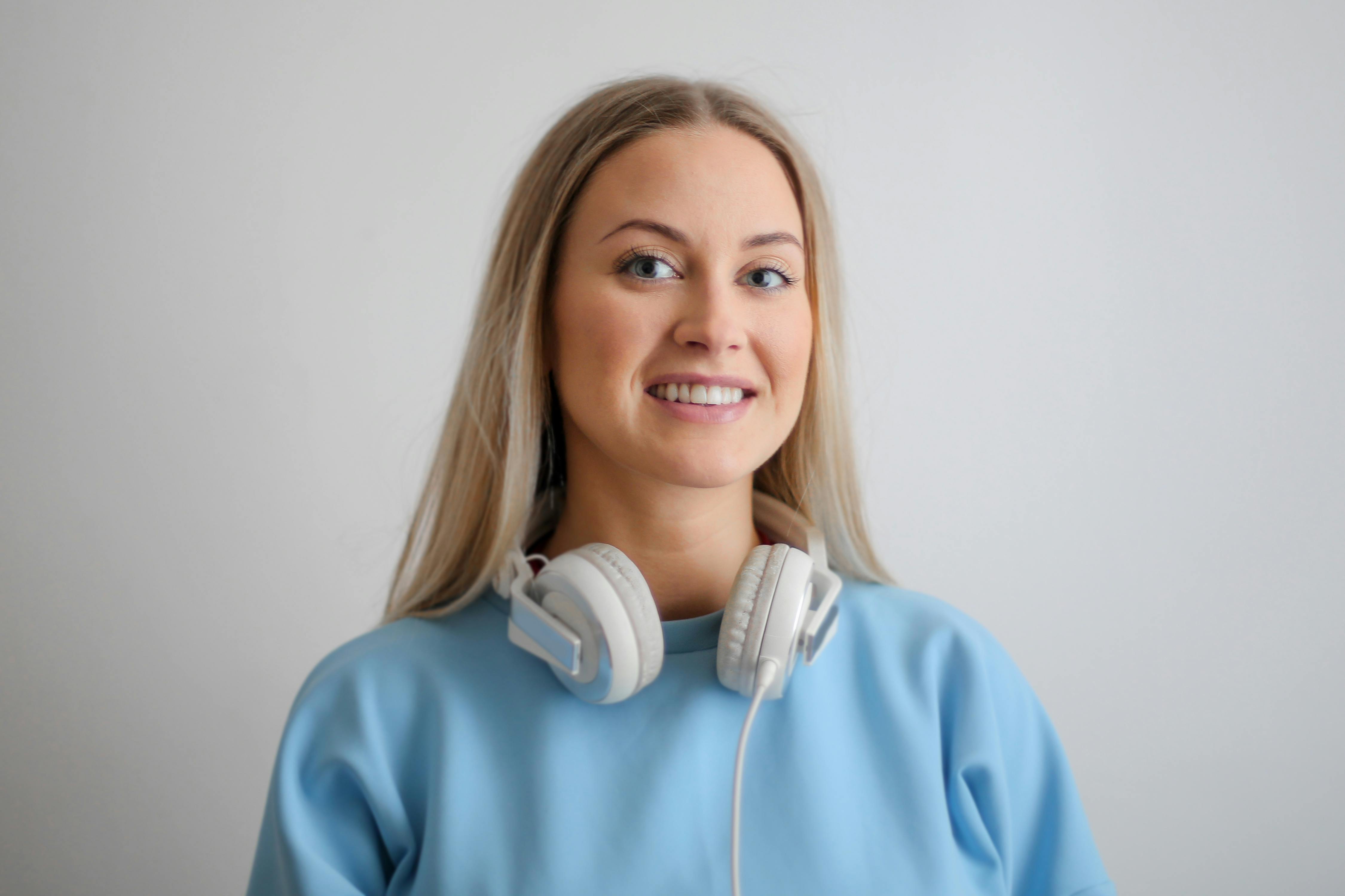 headshot of smilling young female business owner waering headphones around neck and wearing a skyblue jumper